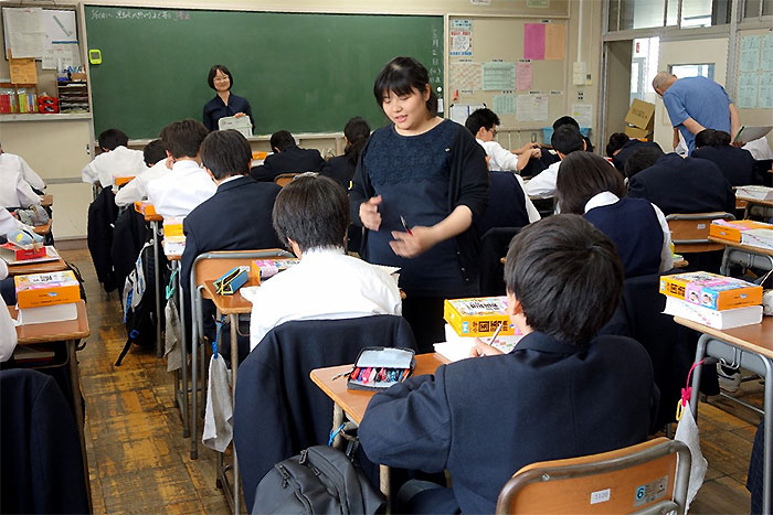 教室の中、どの子の机にも国語辞典が乗っている。生徒が課題に取り組んでおり、柏野先生が黒板の前にいる。国語科担当の先生が男子生徒に声を掛けている写真