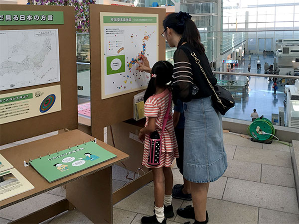 空港ターミナルでモバイルミュージアムのパネルにシールを貼る親子