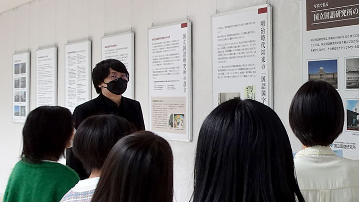 展示パネルの前で国語研の歴史と研究内容を説明する岩崎拓也特任助教