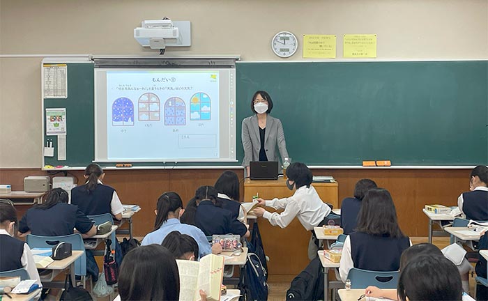 授業風景の写真。中央に柏野准教授がおり、背後のプロジェクターに転記のイラストが写っている。生徒は熱心に辞書を見ている。最前列の生徒は隣の生徒に辞書を見せている