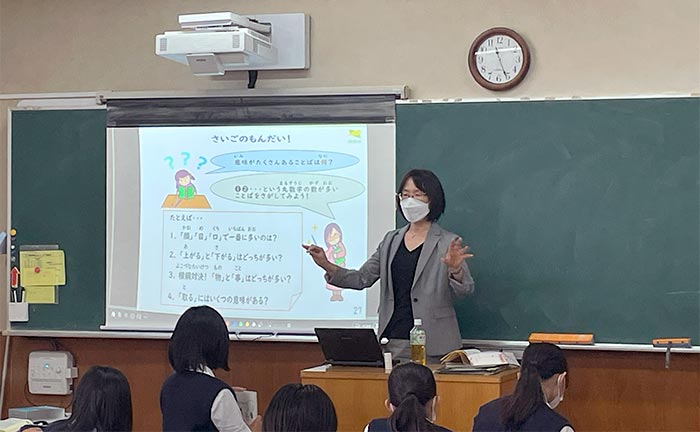 身振りを交えて説明する柏野准教授の写真。背景のプロジェクターには「さいごのもんだい!」のタイトルと「意味がたくさんあることば」についての設問並んでいる