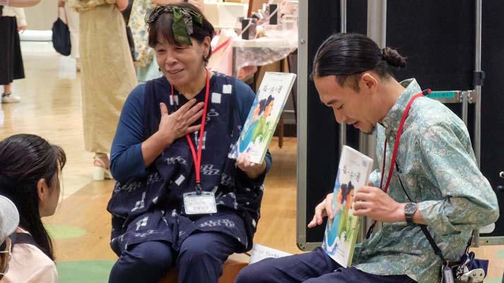 絵本を手に読み聞かせをする沖永良部島の女性と国語研の山田真寛准教授