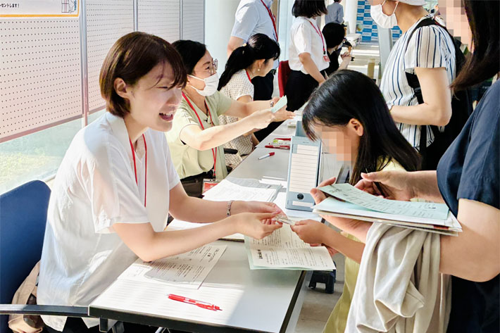 クイズラリーの受付で参加者に問題用紙を手渡しするスタッフ